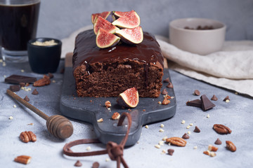 Square chocolate cake with chocolate cream, figs and blackberries on a gray background. Cold coffee in a glass and pine nuts.
