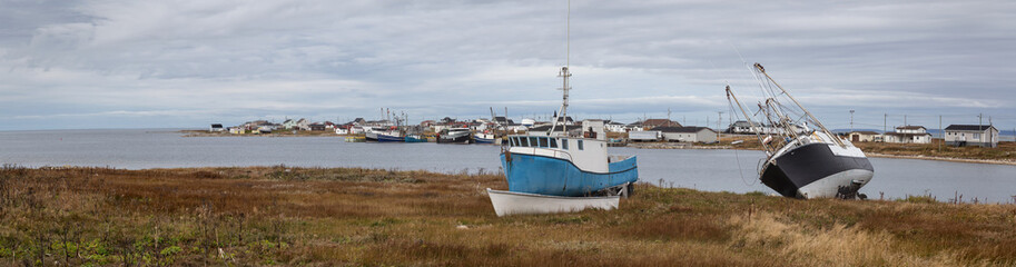 Fototapeta premium Panoramic view on the small town on the Atlantic Ocean shore with boats parked onshore. Taken in Flower's Cove, Newfoundland and Labrador, Canada.
