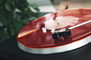 Turntable vinyl record player on a white background. Retro audio equipment for disc jockey. Sound technology for DJ to mix & play music. Red vinyl record and needle. Indoor green plant in a white pot