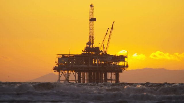 Silhouette of Oil rig coastal platform at sunset drilling for fuel Pacific coastline slow motion California USA  
