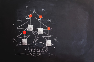 A cup of tea and a Christmas tree decorated with tea bags. Drawing on chalk board.