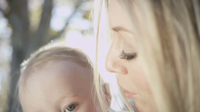 Portrait of loving beautiful blonde European mother with her young baby boy outdoors in the park 