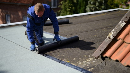 Dachdecker Facharbeiter auf Flachdach Baustelle mit Bitumen Dachpappe Baumaterial beim Abkleben vom Hallendach Haus - obrazy, fototapety, plakaty