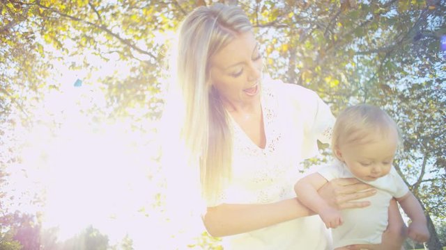 Smiling attractive blonde young Caucasian mother having fun with her baby boy outdoors in the sunshine 