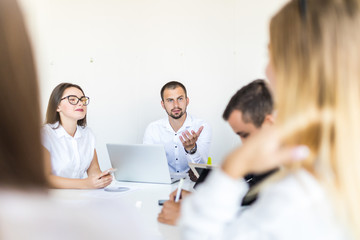 Fototapeta premium Successful team leader and business owner leading informal in-house business meeting. Businessman working on laptop in foreground. Business and entrepreneurship concept.