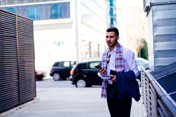 Businessman is standing in the city center near the cafe and looking interested in his notebook.