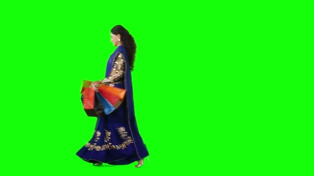 Happy Indian woman walking in the studio while carrying shopping bags and wearing saree clothes. Shot in 4k resolution