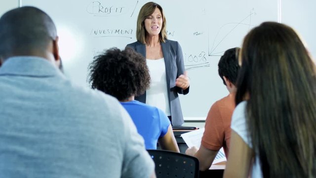 Caucasian American female tutor lecturing class multi ethnic mature students in modern classroom  