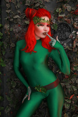 Fototapeta na wymiar beautiful young woman with red hair posing in green costume near the leaves