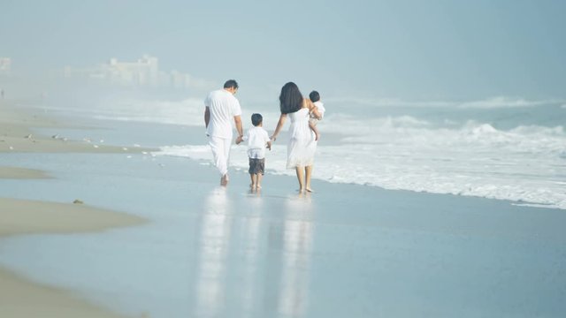 Happy Young Ethnic Latino Family Enjoying The Ocean Waves Walking By The Coast On Vacation 