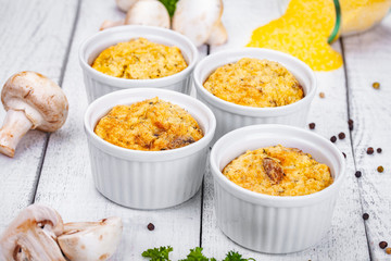 Polenta with mushrooms in white ramekin bowls on wooden rustic table. Close up