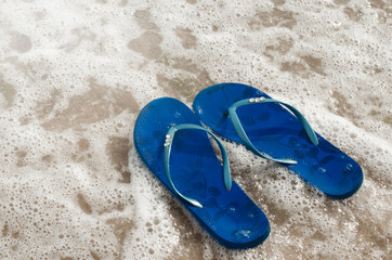 Fototapeta na wymiar flip flops on the beach. sea ​​foam. beach slaps washed away by a wave in the sea
