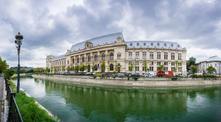 Fototapeta na wymiar Panoramic view of Palace of Justice in downtown Bucharest reflected in Dambovita River; dramatic cloudy sky in the background, Bucharest, Romania
