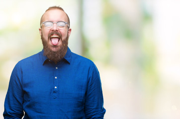 Young caucasian hipster man wearing glasses over isolated background sticking tongue out happy with funny expression. Emotion concept.