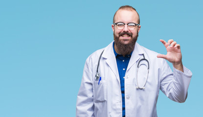 Young caucasian doctor man wearing medical white coat over isolated background smiling and confident gesturing with hand doing size sign with fingers while looking and the camera. Measure concept.