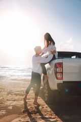 A young couple with a pick up truck on a deserted beach.young couple by pick-up truck parked on...