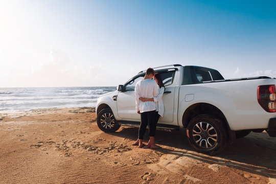 A young couple with a pick up truck on a deserted beach.young couple by pick-up truck parked on beach