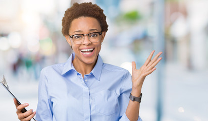 Young african american businesss woman holding clipboard over isolated background very happy and excited, winner expression celebrating victory screaming with big smile and raised hands
