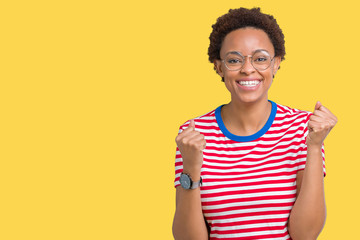 Beautiful young african american woman wearing glasses over isolated background celebrating surprised and amazed for success with arms raised and open eyes. Winner concept.