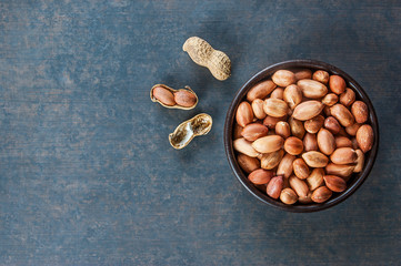 Top view Peanut in nutshell in brown bowl on  rustic wooden background . Composition of peanuts serving to make oil, peanut butter. Great for healthy and dietary nutrition. Concept of condiments

