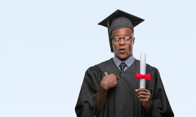 Young graduated african american man holding degree over isolated background with surprise face pointing finger to himself