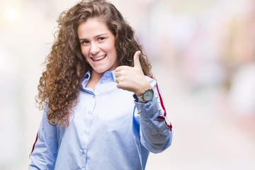 Beautiful brunette curly hair young girl wearing elgant look over isolated background doing happy thumbs up gesture with hand. Approving expression looking at the camera with showing success.