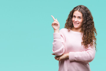 Fototapeta premium Beautiful brunette curly hair young girl wearing pink winter sweater over isolated background with a big smile on face, pointing with hand and finger to the side looking at the camera.
