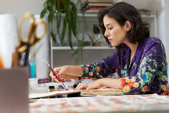 Female Artist Using Paintbrush On Book In Art Studio