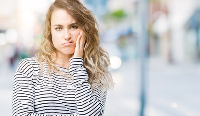 Beautiful young blonde woman wearing stripes sweater over isolated background thinking looking tired and bored with depression problems with crossed arms.