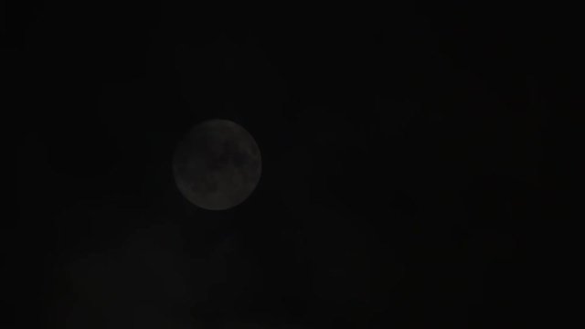 Close shot on bright full moon with clouds, smoke or fog passing by night sky.