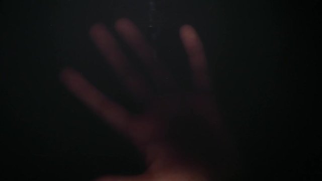 male hand smoothly appears from black water, slowly rotating with fingers and hand. mystical scene with a man hand in black water, the hand of a drowned man. white hand silhouette on black background.