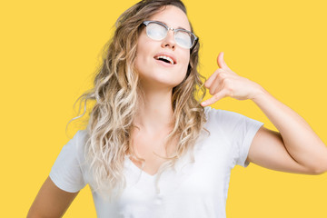 Beautiful young blonde woman wearing glasses over isolated background smiling doing phone gesture with hand and fingers like talking on the telephone. Communicating concepts.