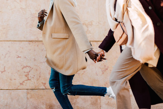 Closeup of multiethnic couple holding hands running on the street. 