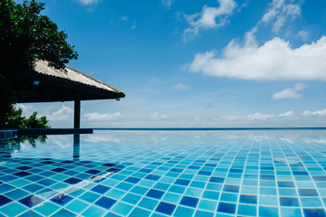 Infinite swimming pool with reflection of ocean and clouds in the water