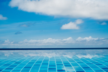 Infinite swimming pool with reflection of ocean and clouds in the water