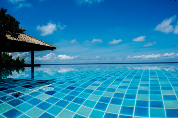 Infinite swimming pool with reflection of ocean and clouds in the water