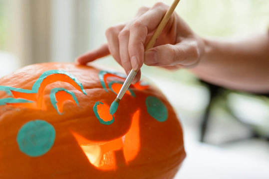 Woman paints face onto a Halloween jack-o-lantern