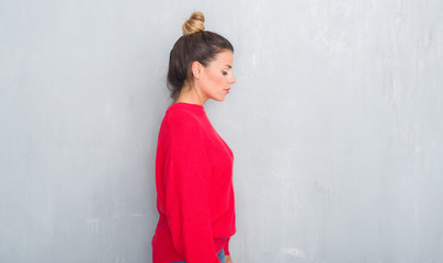 Young adult woman over grey grunge wall wearing winter outfit looking to side, relax profile pose with natural face with confident smile.