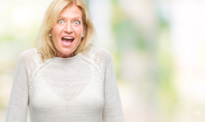 Middle age blonde woman wearing winter sweater isolated background afraid and shocked with surprise expression, fear and excited face.