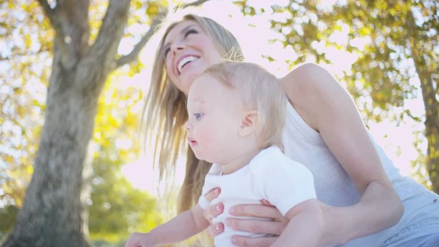 Portrait of attractive blonde Caucasian mom and her young baby boy enjoying togetherness outdoors in the park 