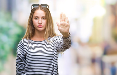 Young beautiful blonde woman wearing sunglasses over isolated background doing stop sing with palm of the hand. Warning expression with negative and serious gesture on the face.