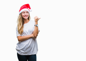 Fototapeta na wymiar Young beautiful blonde woman wearing christmas hat over isolated background smiling with happy face looking and pointing to the side with thumb up.
