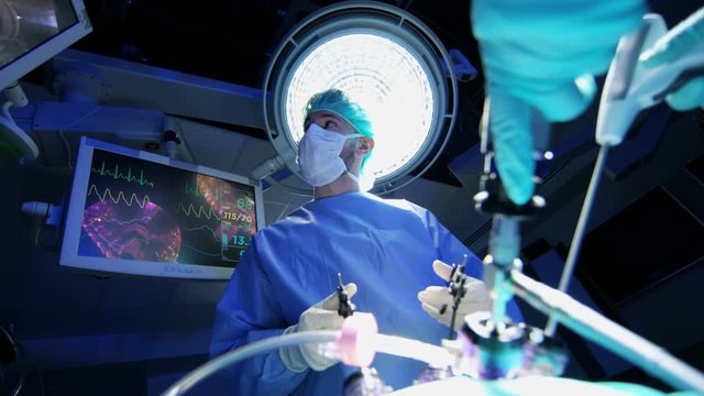 Medical European Caucasian surgical team in scrubs performing Laparoscopy surgery on the patient in operating theatre using video camera technology  