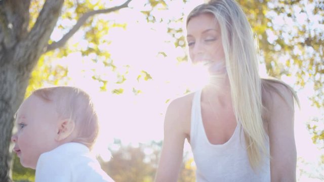 Cute blonde European mom and her young baby boy enjoying togetherness outdoors in the park 