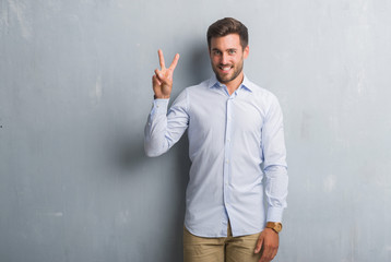 Handsome young business man over grey grunge wall wearing elegant shirt showing and pointing up with fingers number two while smiling confident and happy.