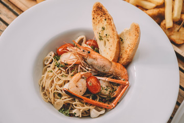 spaghetti pasta with shrimps and sweet basil on white plate over wooden table