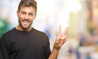 Young handsome man over isolated background smiling with happy face winking at the camera doing victory sign. Number two.