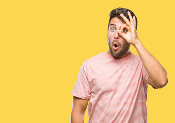 Obraz premium Young handsome man over isolated background doing ok gesture shocked with surprised face, eye looking through fingers. Unbelieving expression.