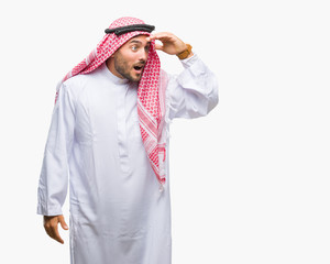 Young handsome man wearing keffiyeh over isolated background very happy and smiling looking far away with hand over head. Searching concept.