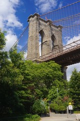 Brooklyn, New York, USA: The Brooklyn Bridge (1883) on a sunny day, surrounded by trees, looking upward from Brooklyn Bridge Park.